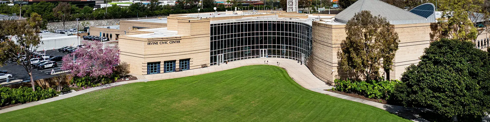 Irvine City Hall, a Modern tan building with large glass entrance, green lawn, and trees under a blue sky.