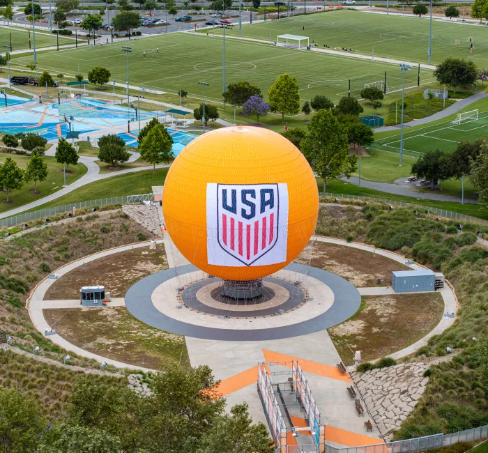 Large orange sphere with USA logo in a circular park, surrounded by green sports fields.