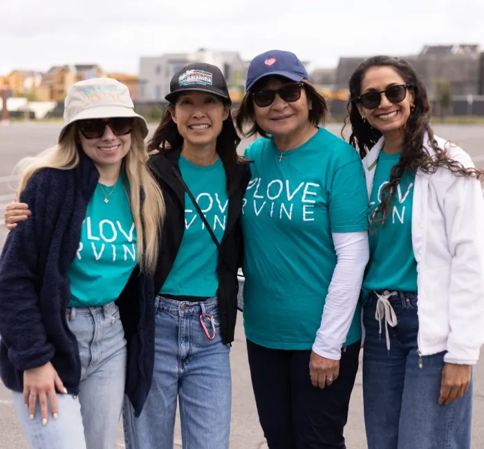 Four smiling women in teal "LOVE IRVINE" shirts stand in a parking lot.