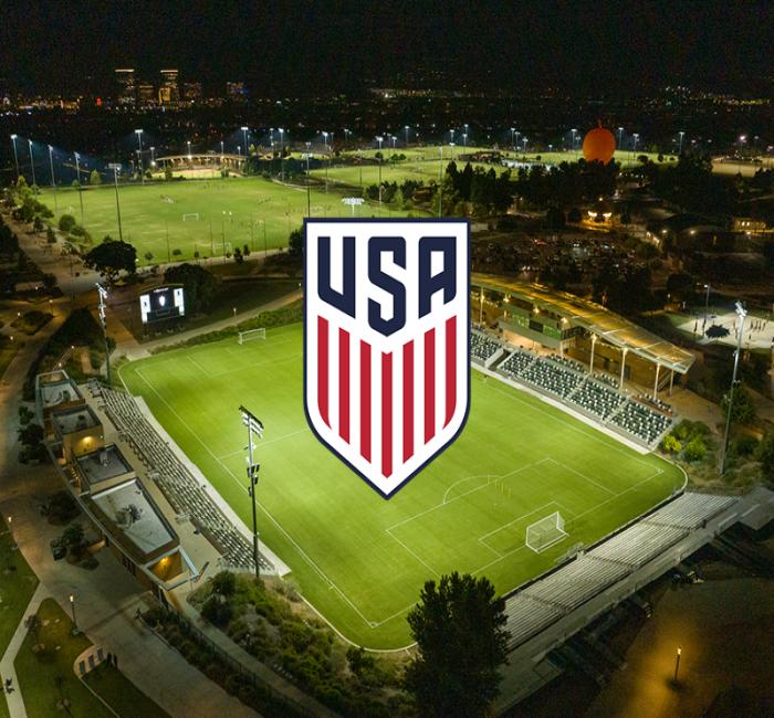 USA soccer logo over a brightly lit stadium at night, with city lights in background.