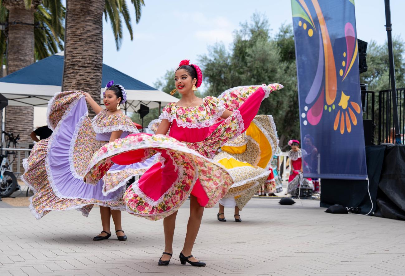 Two young girls in vibrant floral dresses perform a folkloric dance outdoors.