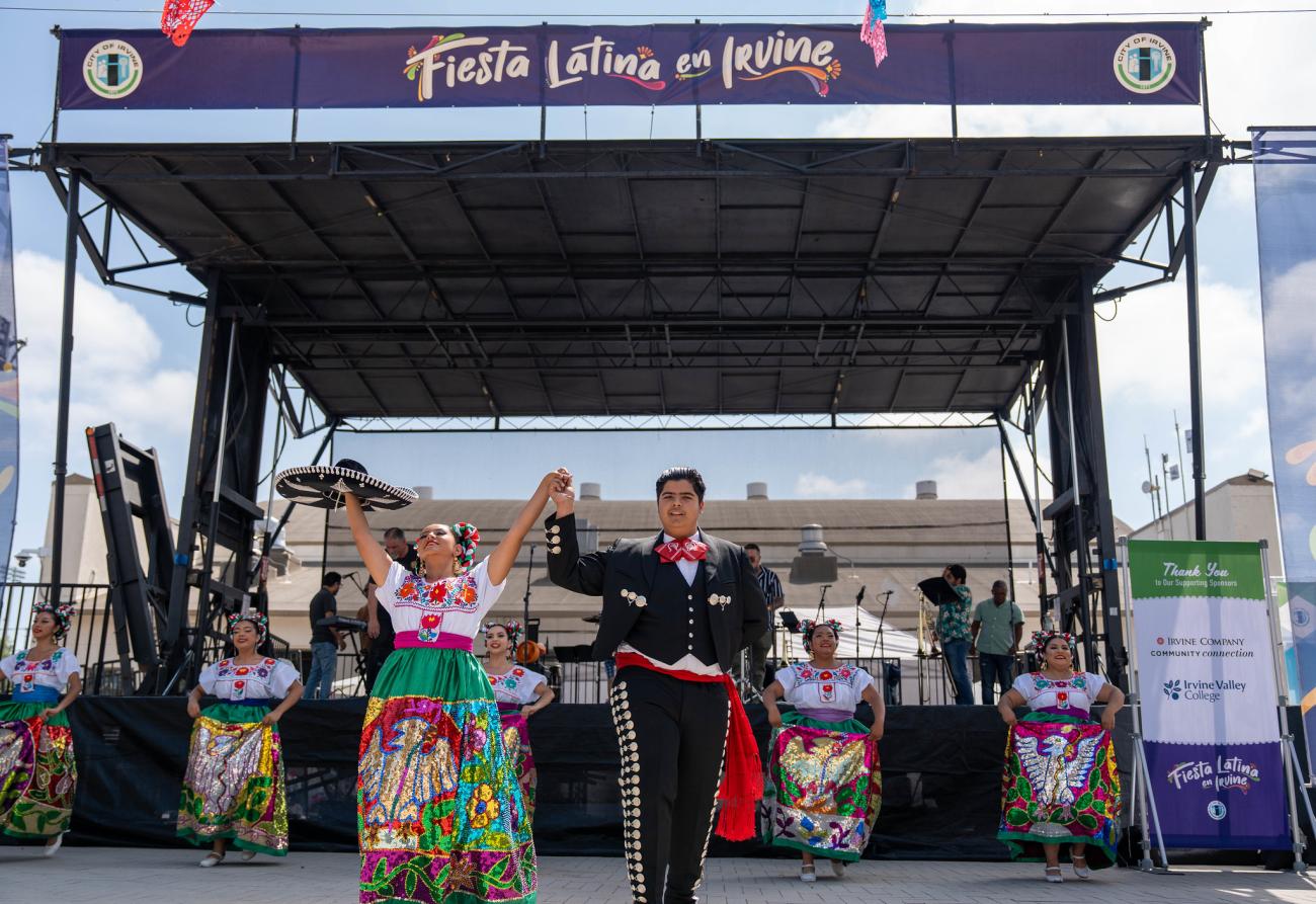 Folk dancers in colorful traditional costumes perform on an outdoor stage at Fiesta Latina.