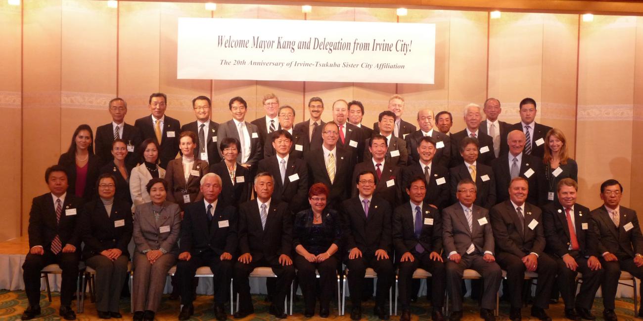 Group photo: 40+ professionals, mostly men in suits, posed at a formal event with a banner.