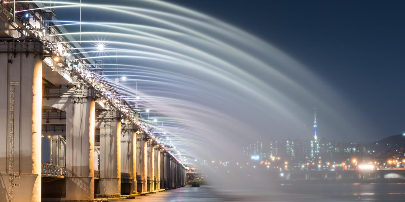 Banpo Bridge Rainbow Fountain at night, Seoul city skyline in distance.