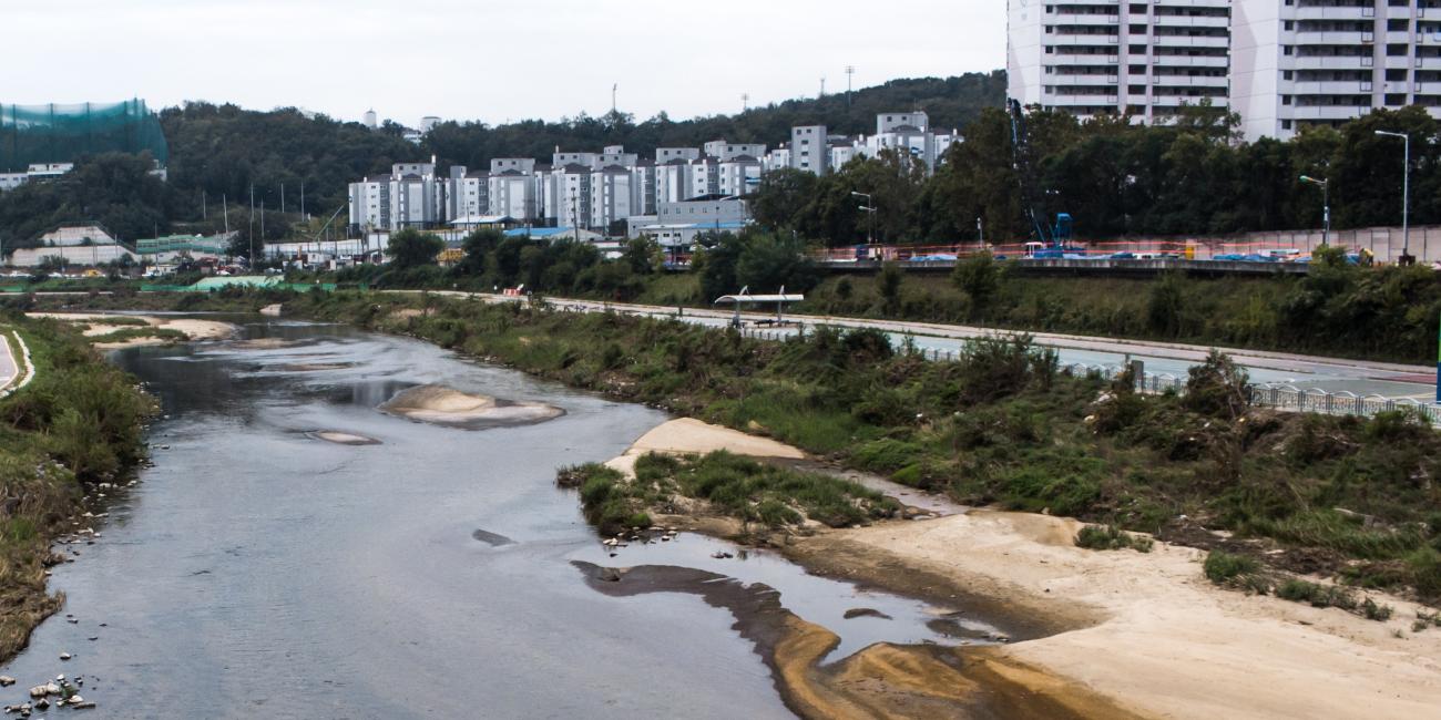 Urban river, sandy banks, roads, green vegetation, and apartment buildings.