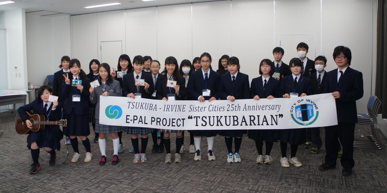 Group of students in uniforms holding "TSUKUBARIAN" project banner, one playing guitar.