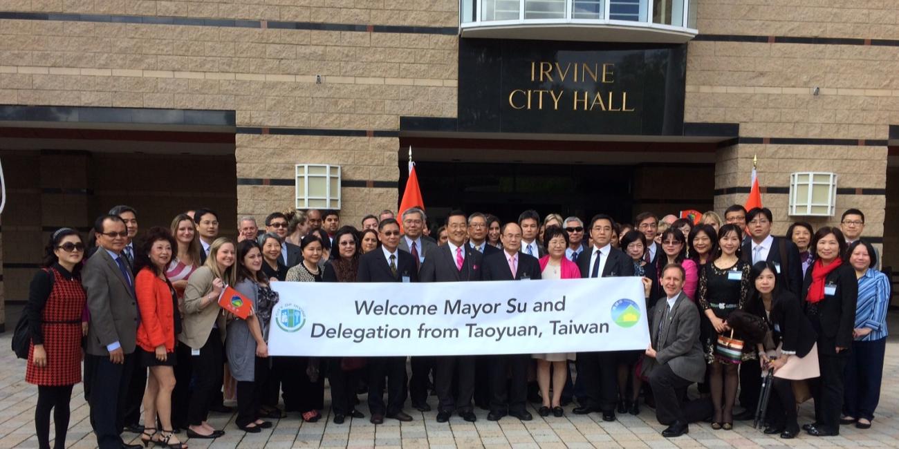Group of adults standing in front of building holding a sign