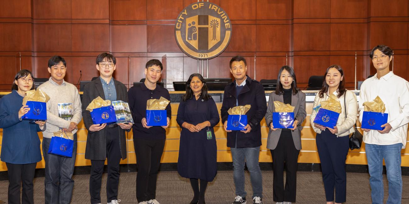 Photograph of smiling adults posing while being presented with blue gift bags