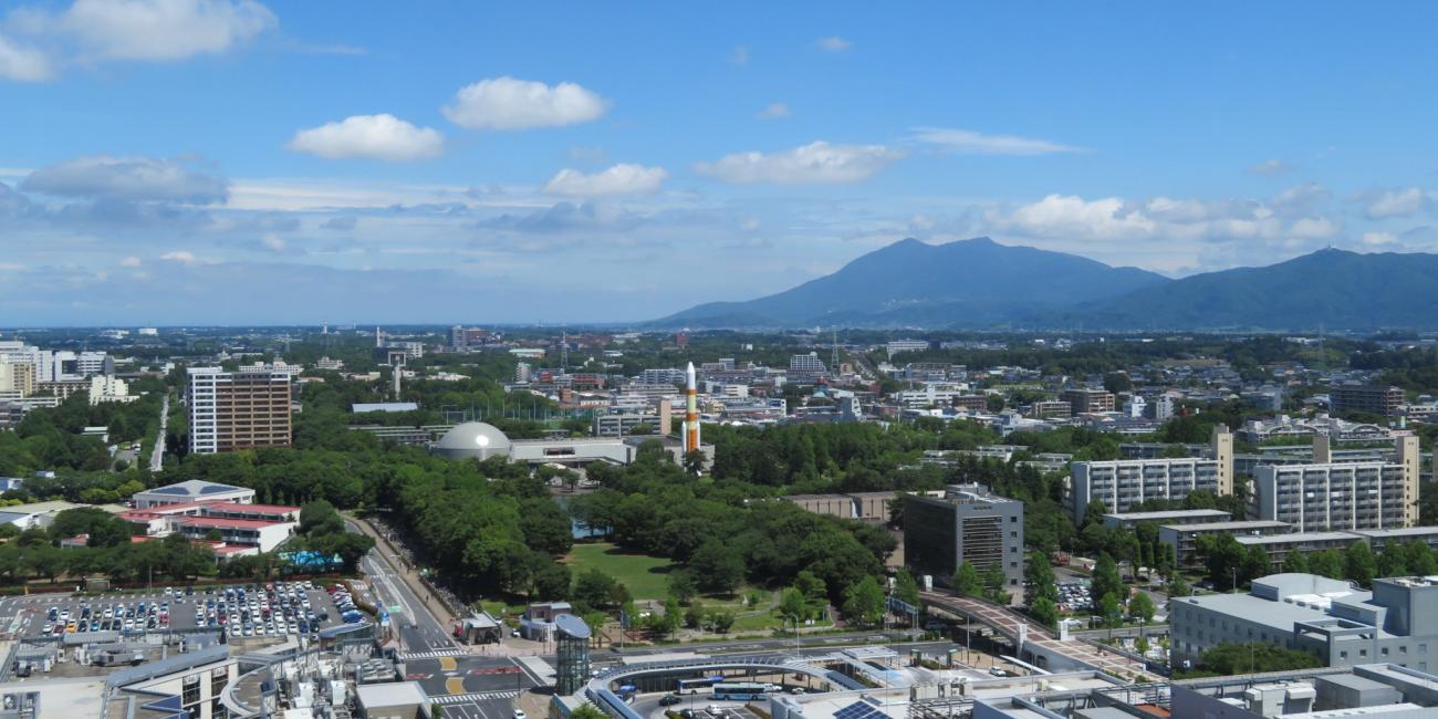 Photograph: Aerial view of a city with green parks, buildings, roads, and mountains under a blue sky.