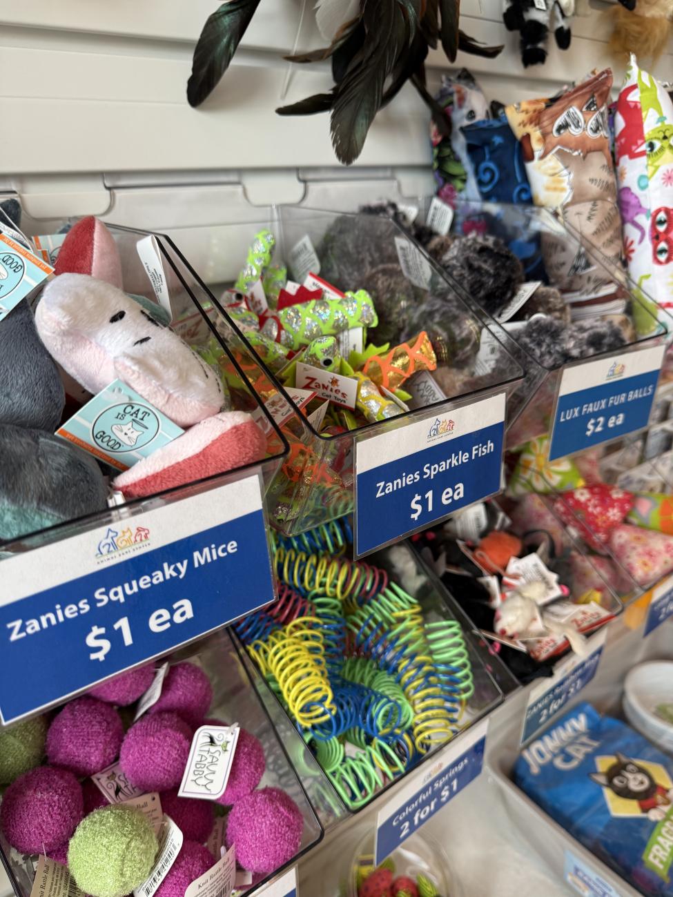 Retail display featuring clear bins overflowing with various colorful pet toys.