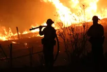 Silhouetted firefighters watching a raging wildfire at night.