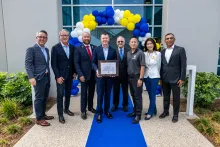 Eight people from SpyGlass Pharma and the Irvine City Council stand in front of a blue and yellow balloon arch. One man holds a certificate