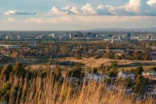 City skyline and suburbs from a grassy hill at golden hour.