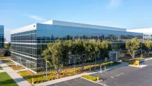 Modern glass office building with trees and landscaping under a blue sky.