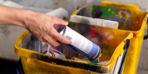 Hand places a spray paint can into a yellow, paint-splattered bucket.