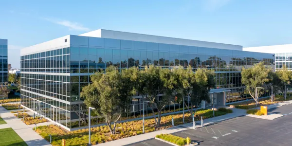 Modern glass office building with trees and landscaping under a blue sky.