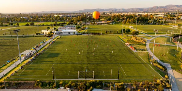 Golden hour aerial view of the Great Park Sports Complex with a soccer game underway and the Great Park Balloon.