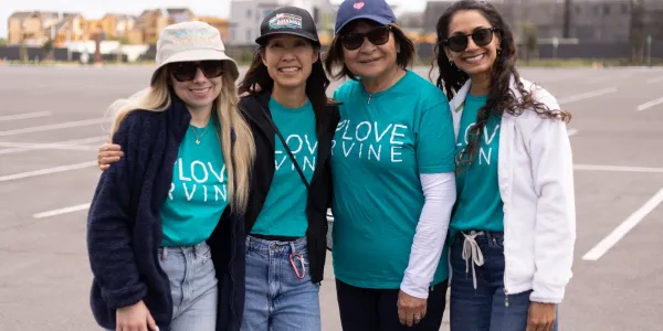 Four smiling women in teal "LOVE IRVINE" shirts stand in a parking lot.