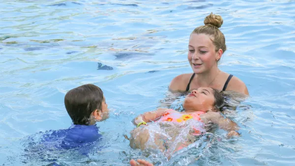 Young woman smiles, supporting a child floating on their back in a swimming pool.
