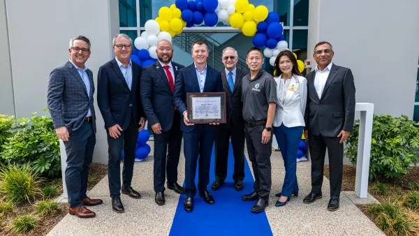 Eight people from SpyGlass Pharma and the Irvine City Council stand in front of a blue and yellow balloon arch. One man holds a certificate