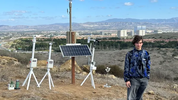 Person stands near scientific instruments and solar panel on a dry hill overlooking a city.