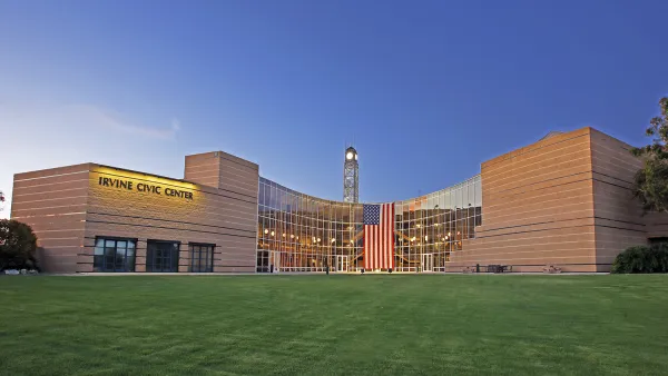 Modern Irvine Civic Center with glass facade, clock tower, and American flag over green lawn.