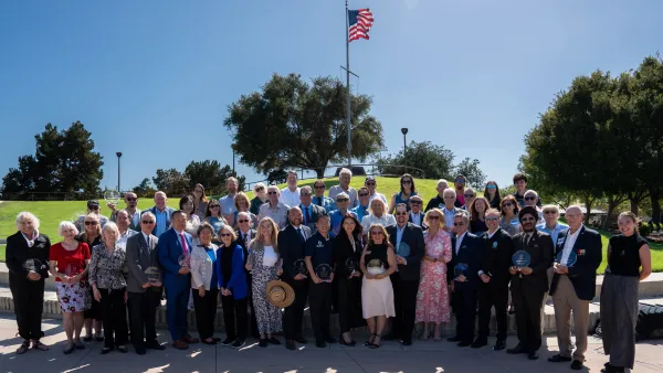 Large group of people holding awards under an American flag on a sunny day.