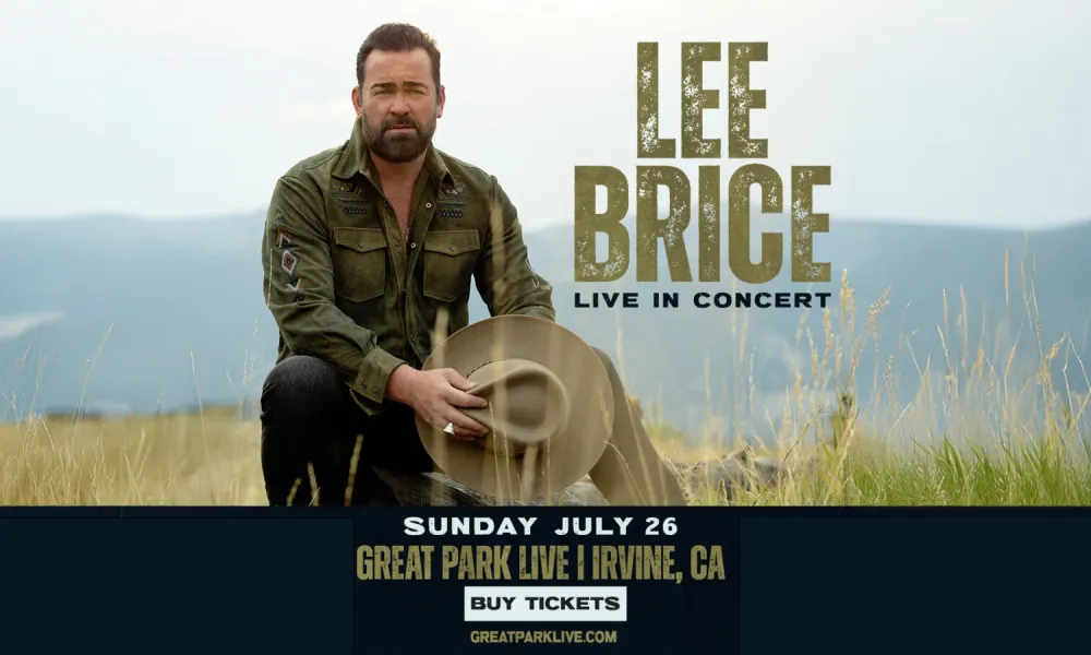 Country singer Lee Brice kneels, holding a cowboy hat in a grassy outdoor scene.
