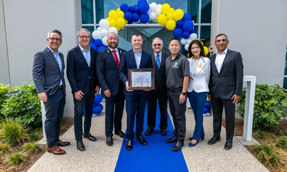Eight people from SpyGlass Pharma and the Irvine City Council stand in front of a blue and yellow balloon arch. One man holds a certificate