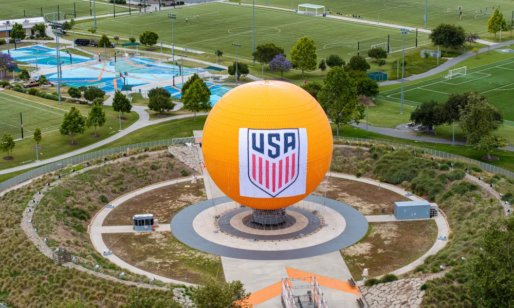 Large orange sphere with USA logo in a circular park, surrounded by green sports fields.