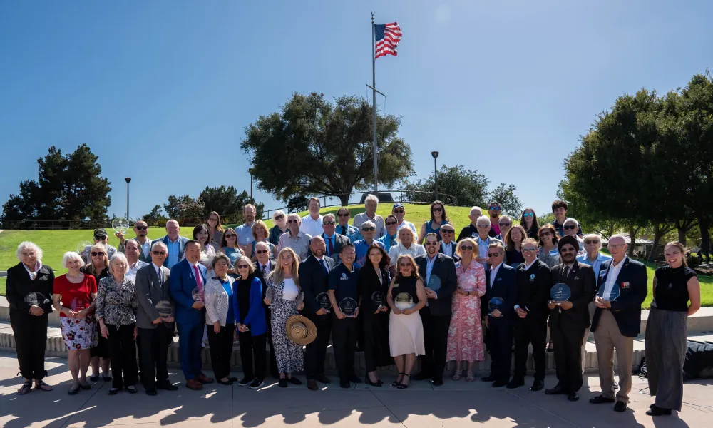 Large group of people holding awards under an American flag on a sunny day.