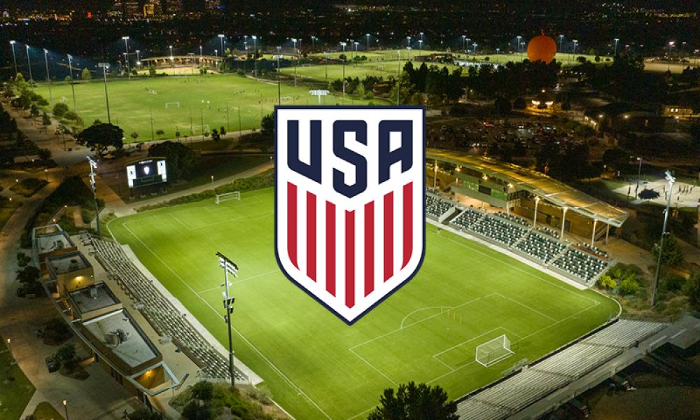 USA soccer logo over a brightly lit stadium at night, with city lights in background.