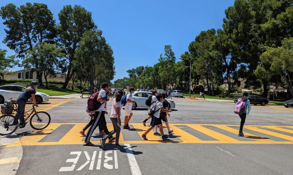 Kids with backpacks walking and riding bikes in a crosswalk