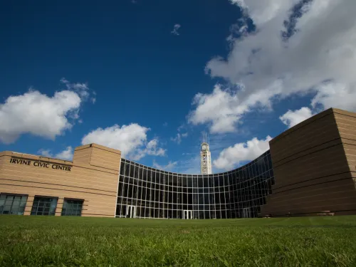 Modern building with curved glass facade, green grass, blue sky with clouds, and a distant tower.