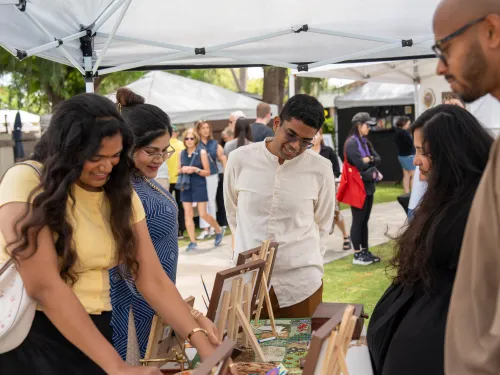 People browse items at an outdoor market stall, smiling.