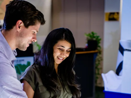 Smiling man and woman collaborate over an illuminated, colorful map on a digital table.