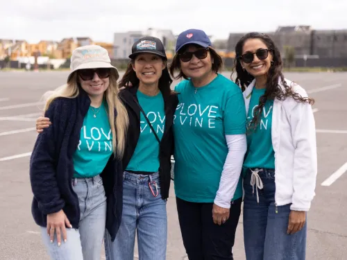 Four smiling women in teal "LOVE IRVINE" shirts stand in a parking lot.