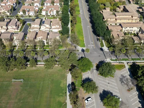 Aerial photo of suburban houses, a wide road, soccer field, and parking lot.