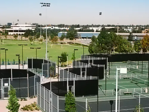 Panoramic view of outdoor sports complex with green paddle courts, fields, and city skyline.
