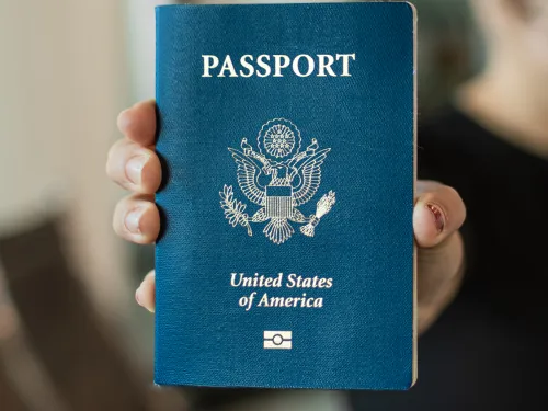 Smiling woman holds a US passport in an airport, luggage beside her.