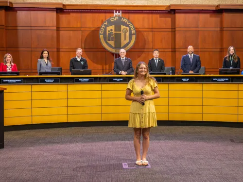 Seven member of City Council standing behind a young woman performing a song as an invocation in the Council Chamber