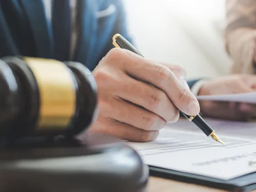 Hand signing a legal document, with a judge's gavel in the foreground.